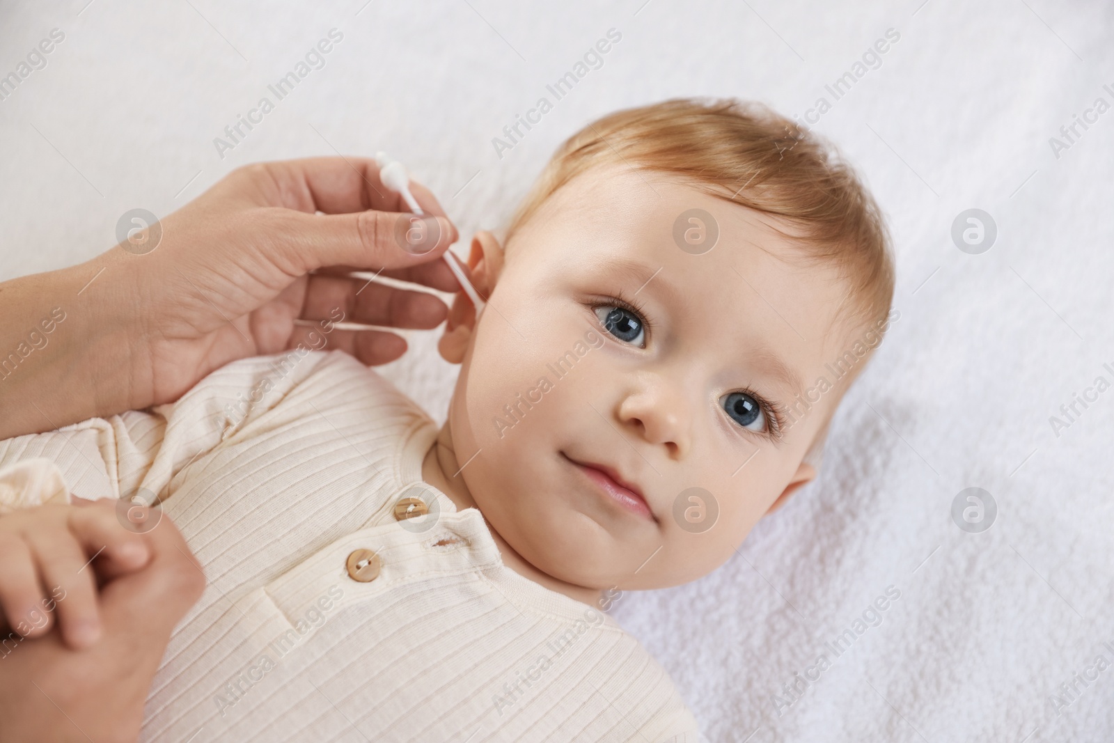 Photo of Mother cleaning ear of her cute little baby with cotton swab on bed, closeup