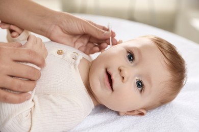 Photo of Mother cleaning ear of her cute little baby with cotton swab on bed, closeup