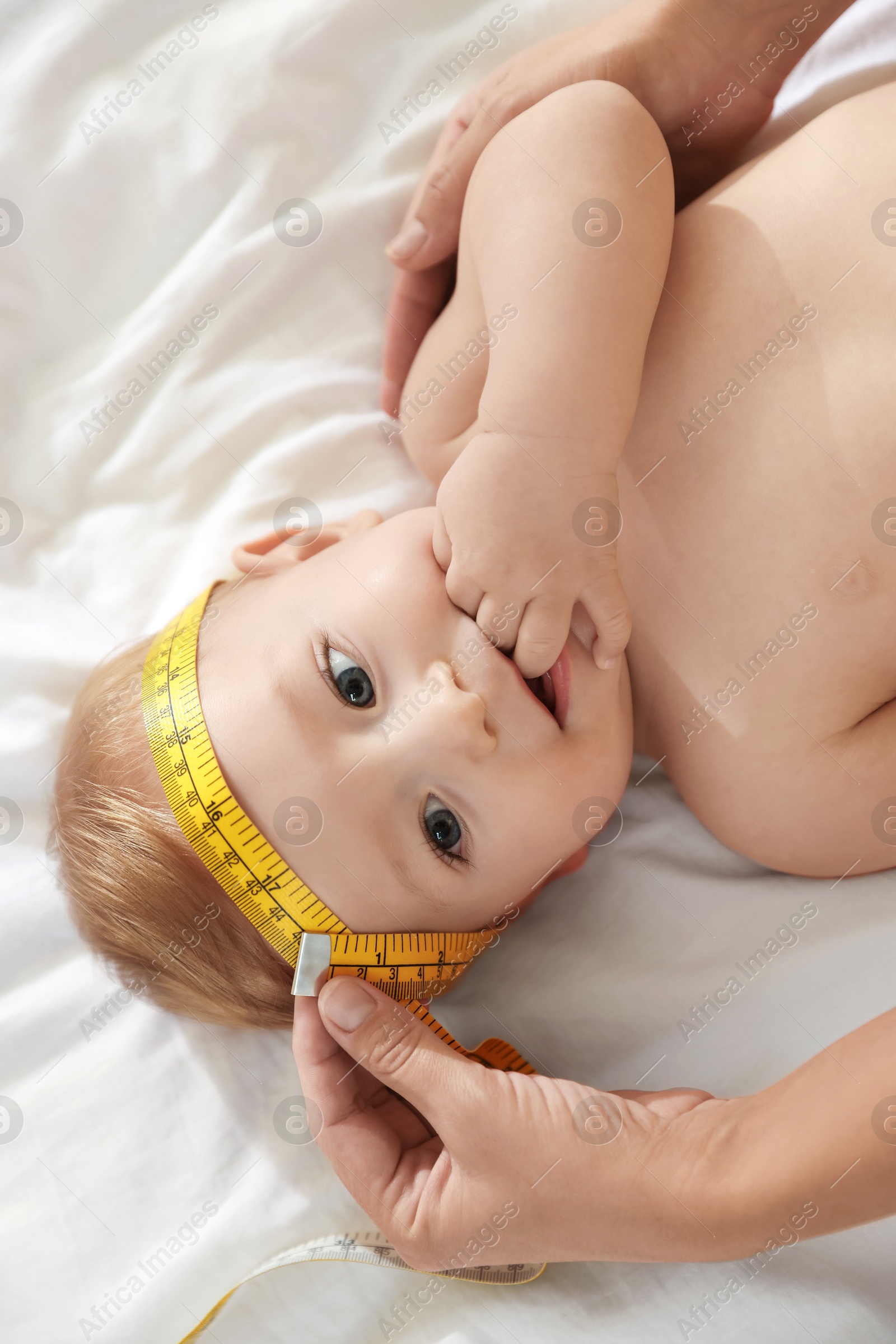 Photo of Mother measuring little baby's head on bed, top view