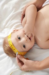 Photo of Mother measuring little baby's head on bed, top view