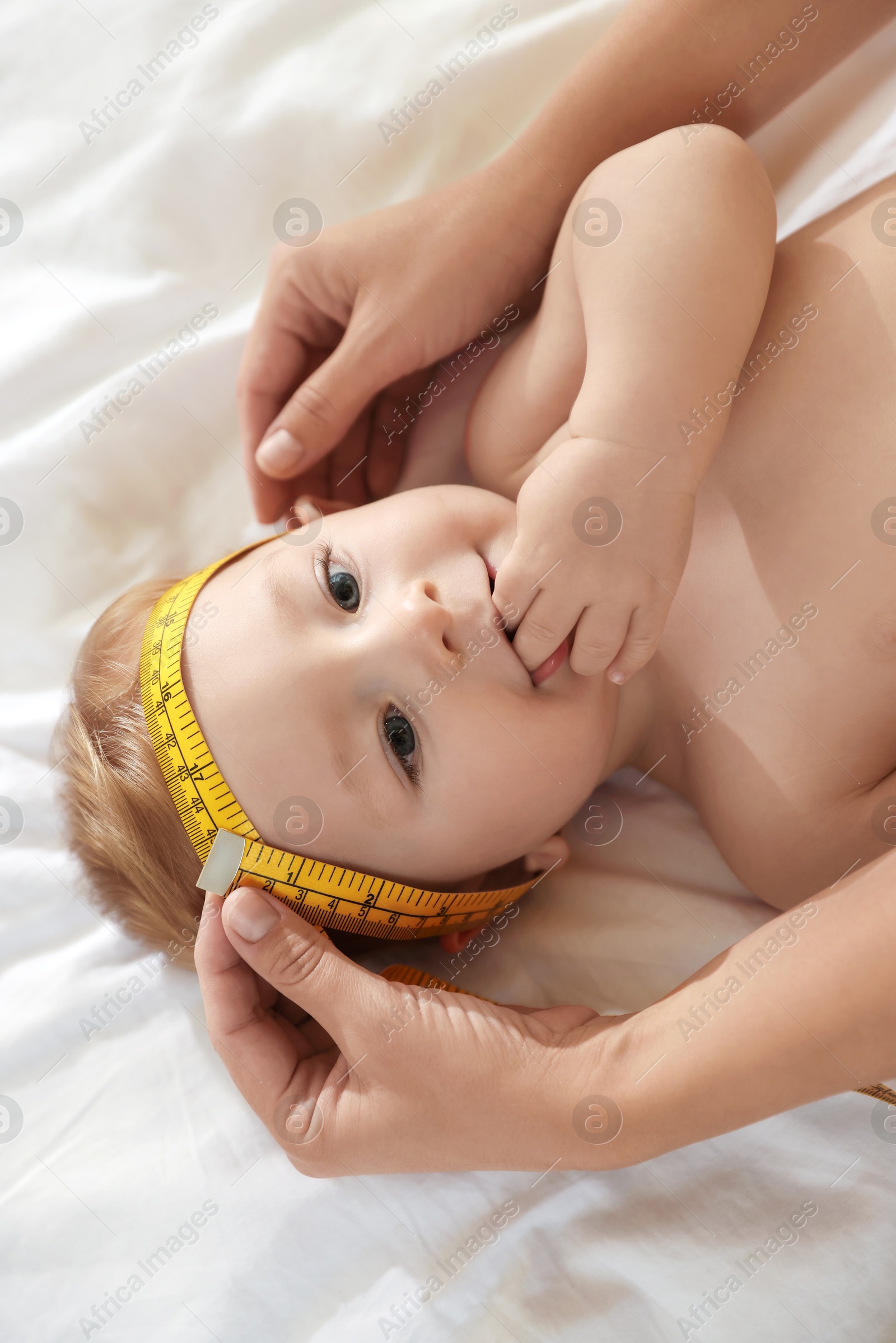 Photo of Mother measuring little baby's head on bed, top view