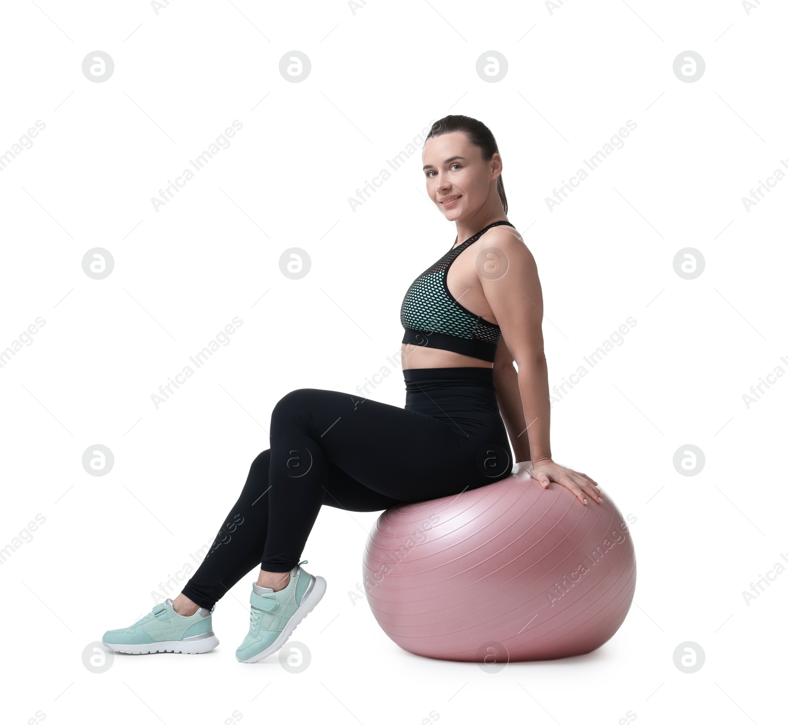 Photo of Smiling woman in sportswear sitting on fitness ball against white background