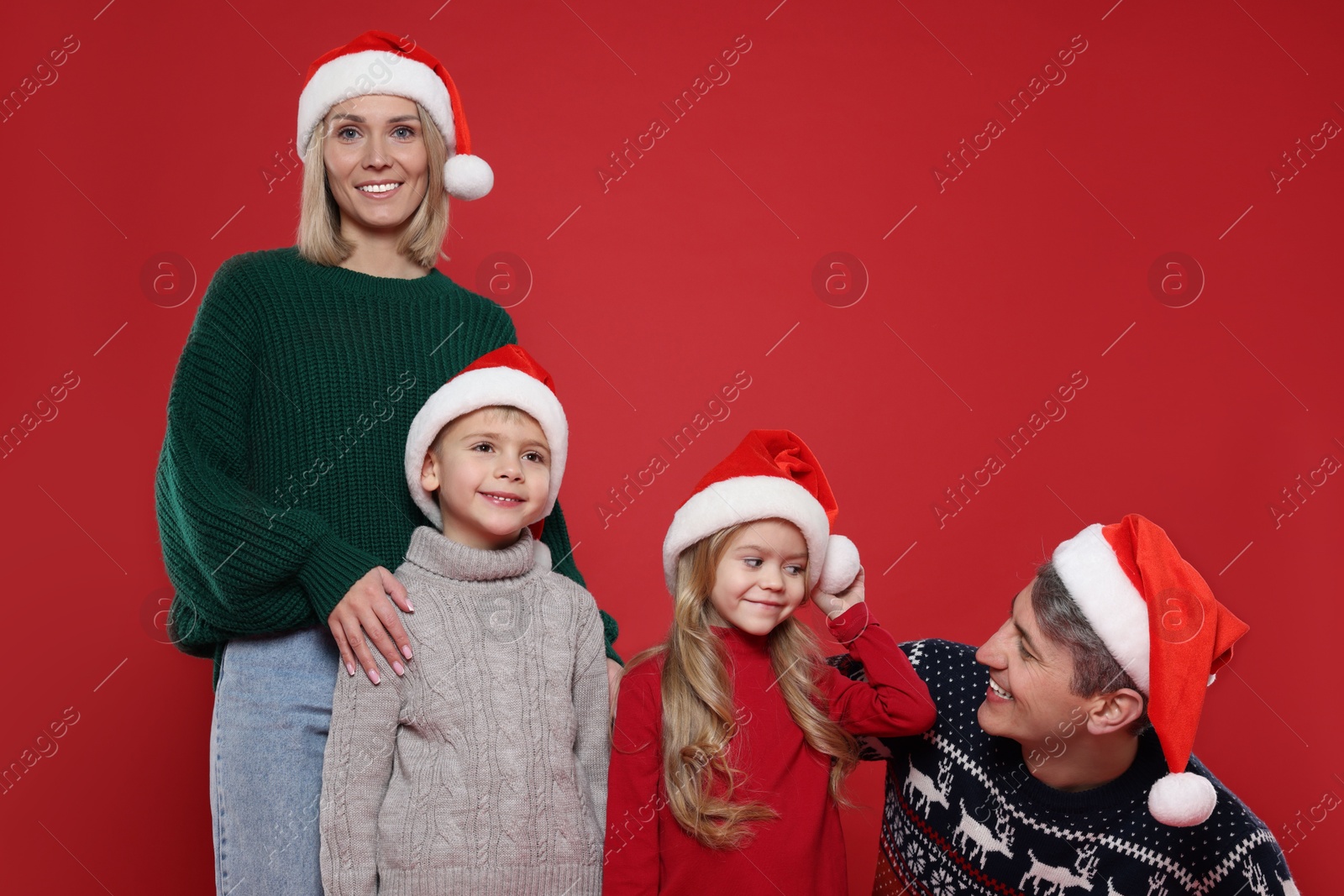 Photo of Happy family in Santa hats on red background. Christmas season