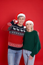 Photo of Happy couple in Santa hats on red background. Christmas celebration