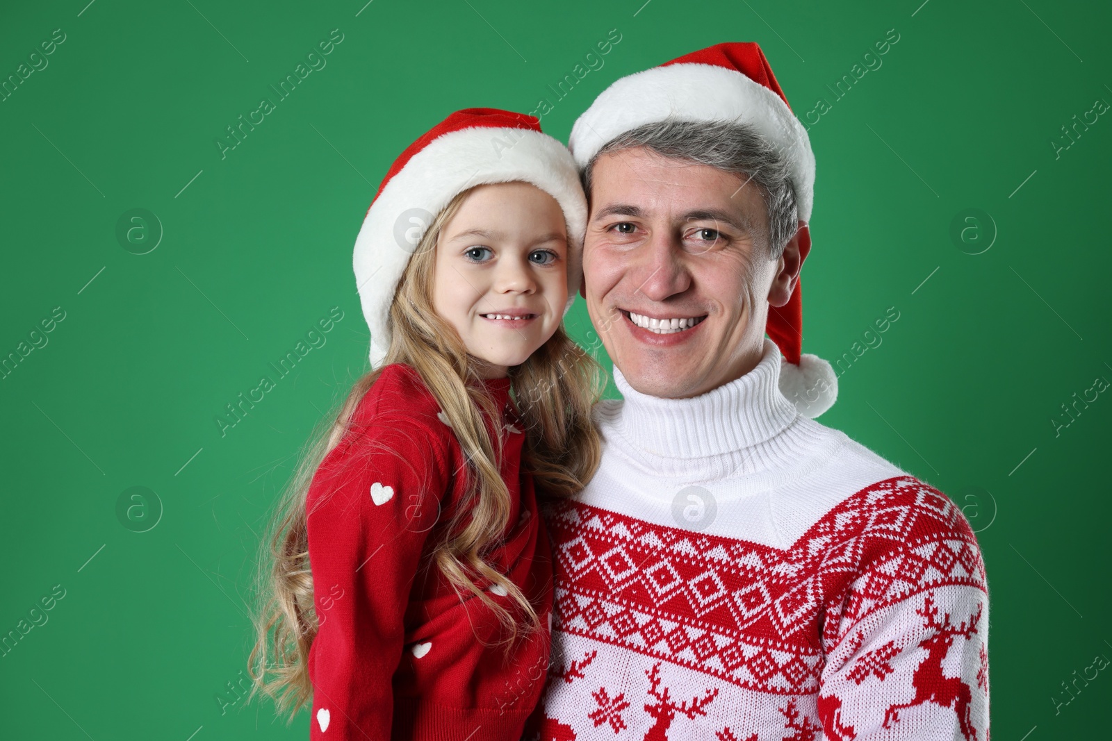 Photo of Father and daughter in Santa hats on green background. Christmas celebration