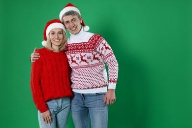 Photo of Happy couple in Christmas sweaters and Santa hats on green background. Space for text