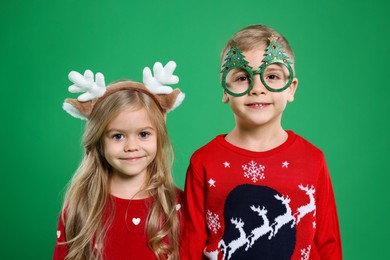 Photo of Cute little children in Christmas sweaters and accessories on green background