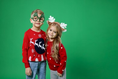 Photo of Cute little children in Christmas sweaters and accessories on green background. Space for text