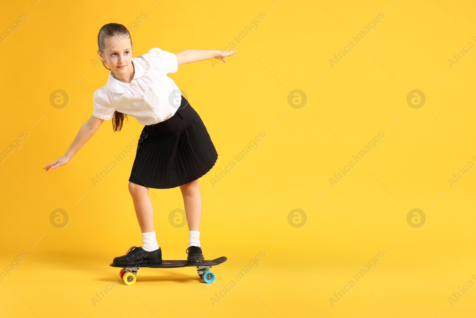 Photo of Little girl standing on penny board against yellow background, space for text