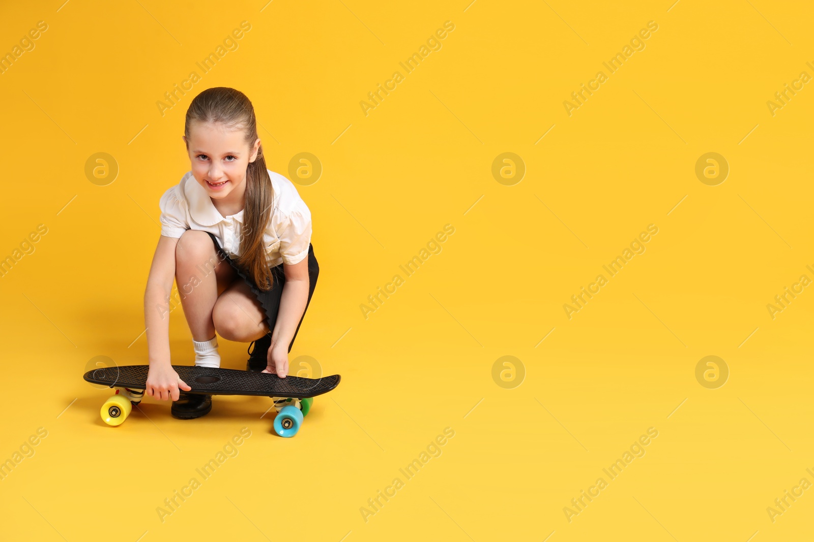 Photo of Little girl with penny board on yellow background, space for text