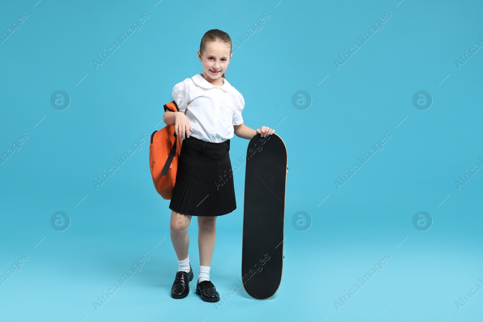 Photo of Little girl with backpack and skateboard on light blue background