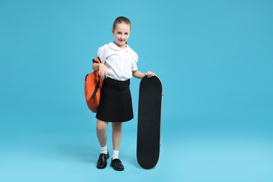 Photo of Little girl with backpack and skateboard on light blue background