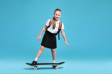 Photo of Little girl with backpack and skateboard on light blue background