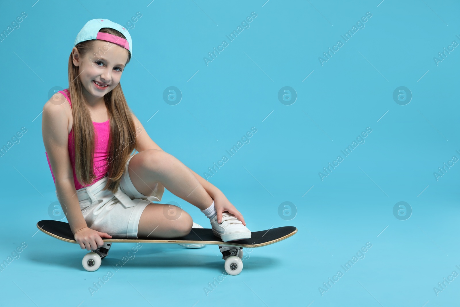 Photo of Stylish girl sitting on skateboard against light blue background, space for text