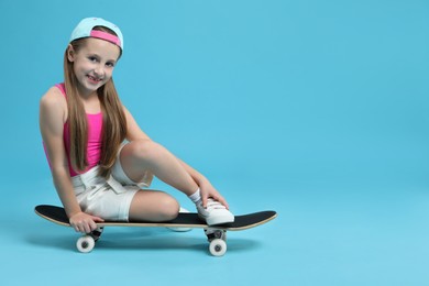 Photo of Stylish girl sitting on skateboard against light blue background, space for text