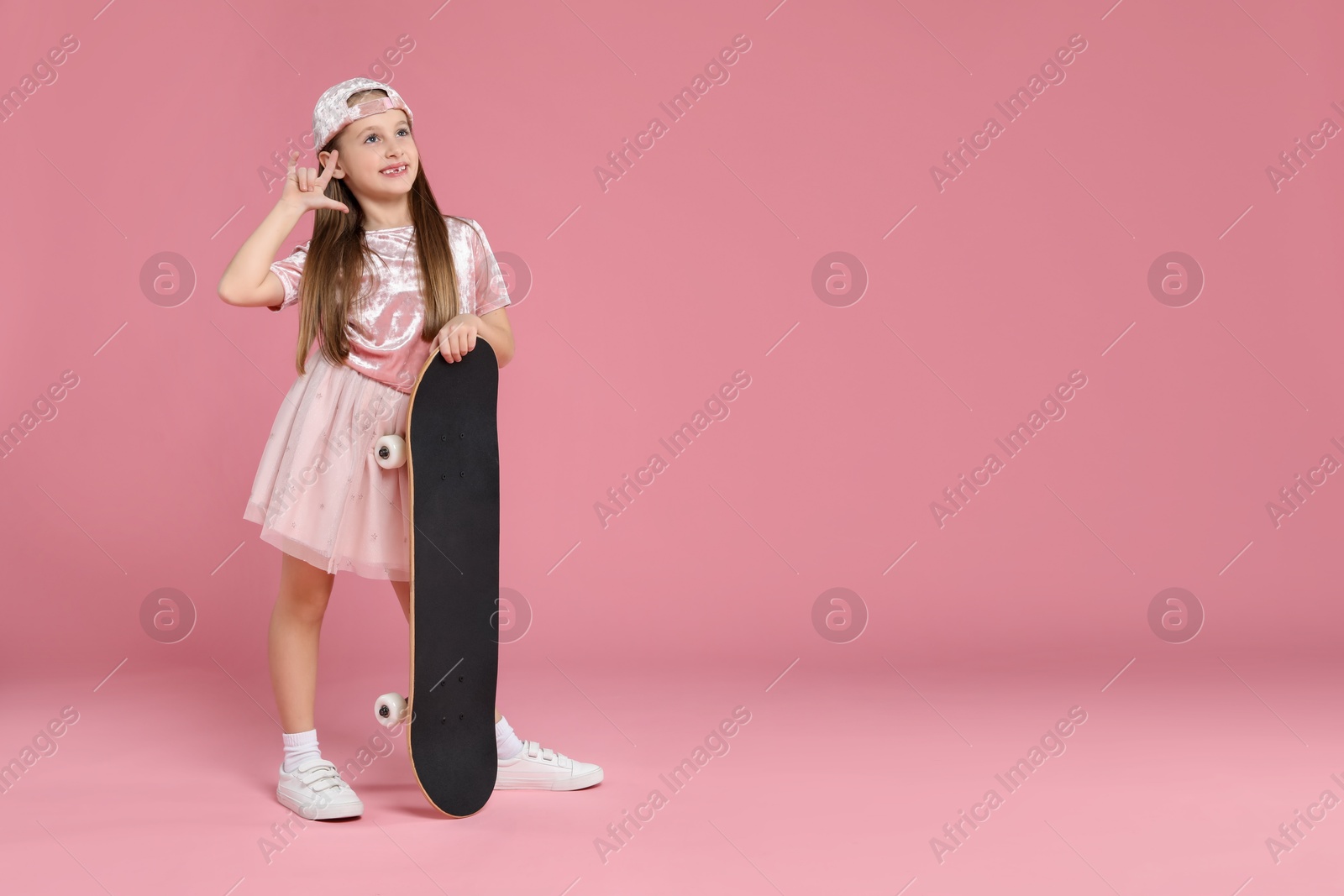 Photo of Little girl with skateboard against pink background, space for text