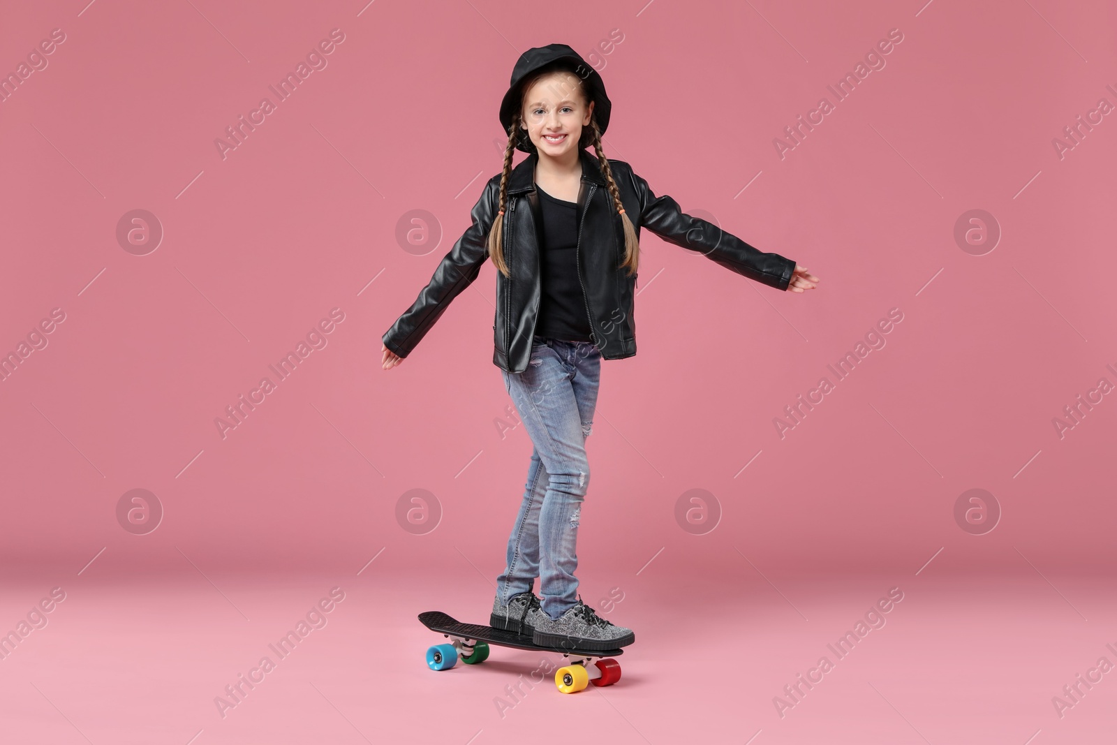 Photo of Little girl standing on penny board against pink background