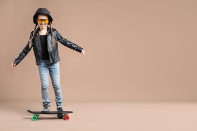 Photo of Little girl with penny board on pale brown background, space for text