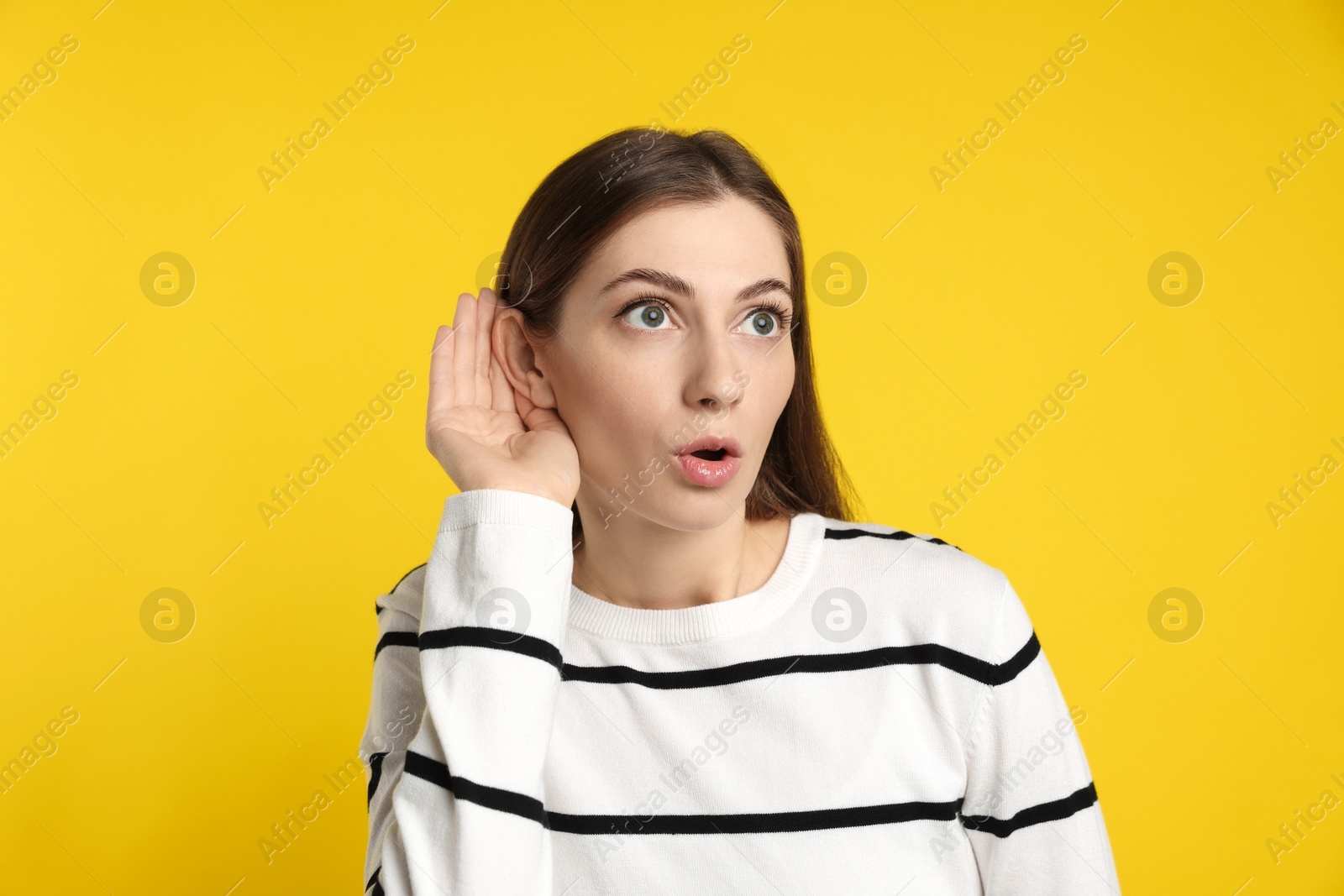 Photo of Woman showing hand to ear gesture on dark yellow background