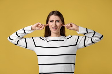 Photo of Woman covering her ears with fingers on dark yellow background