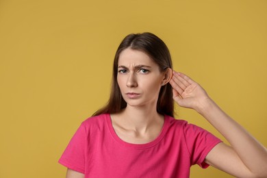 Photo of Woman showing hand to ear gesture on dark yellow background