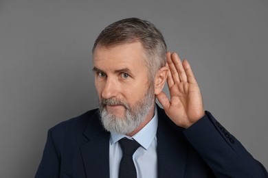 Photo of Senior man showing hand to ear gesture on grey background