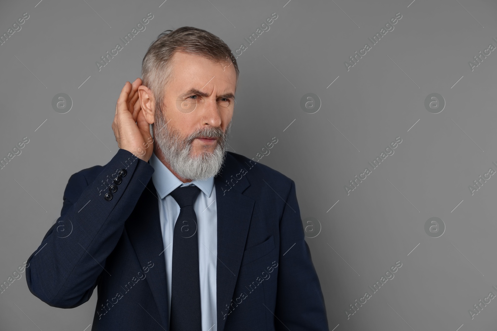 Photo of Senior man showing hand to ear gesture on grey background, space for text