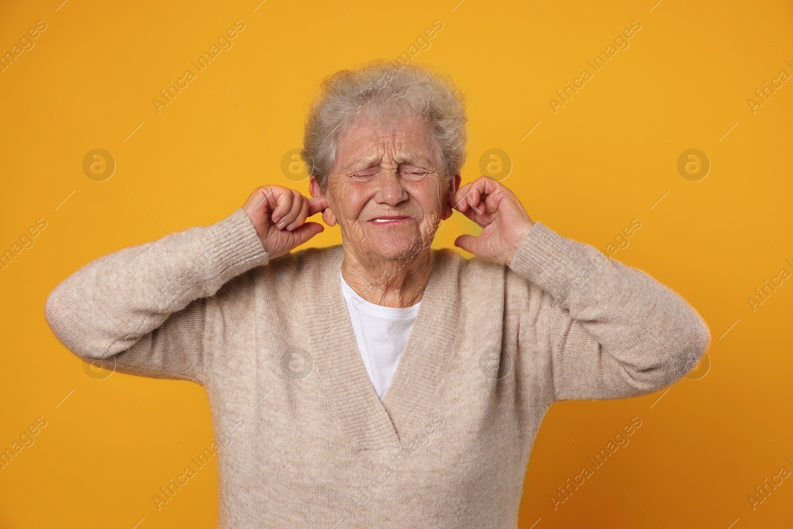 Photo of Senior woman covering her ears with fingers on dark yellow background