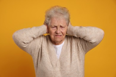 Photo of Senior woman covering her ears on dark yellow background