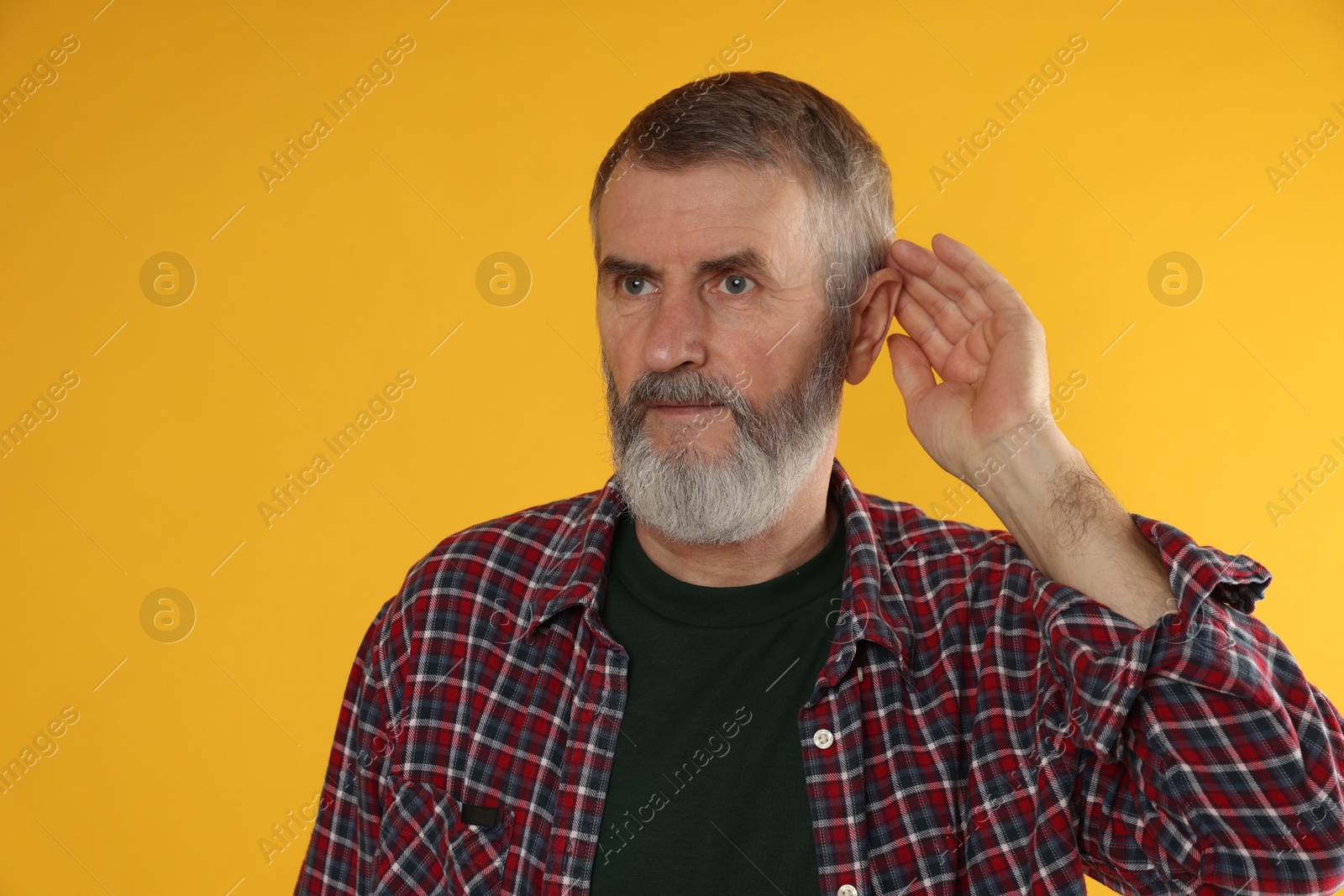 Photo of Senior man showing hand to ear gesture on orange background