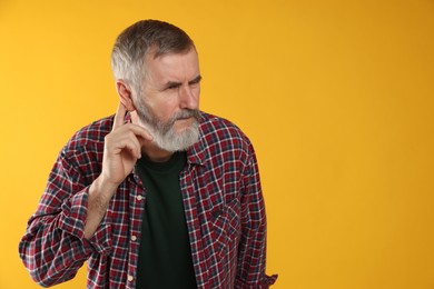 Photo of Senior man showing hand to ear gesture on orange background, space for text