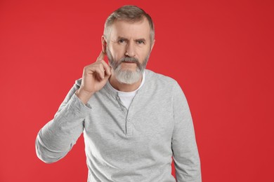 Photo of Senior man showing hand to ear gesture on red background