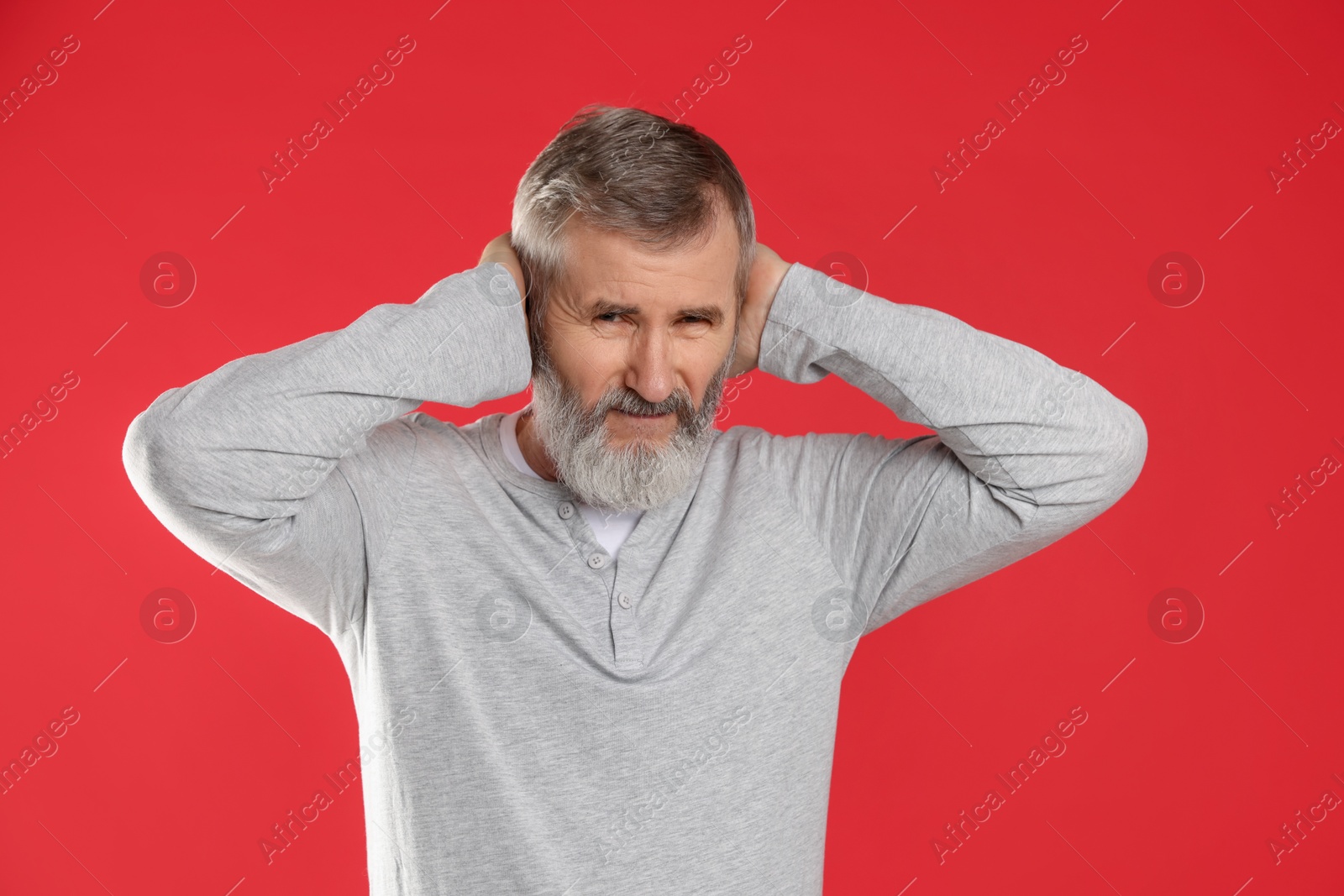 Photo of Senior man covering his ears on red background