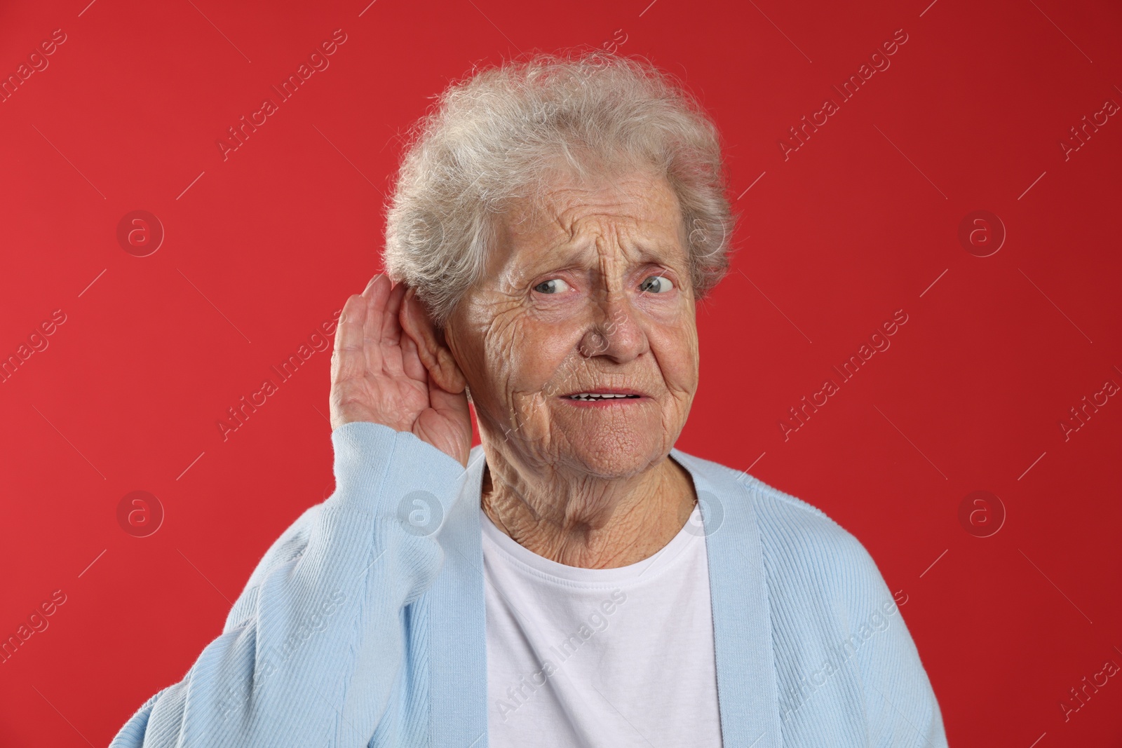 Photo of Senior woman showing hand to ear gesture on red background