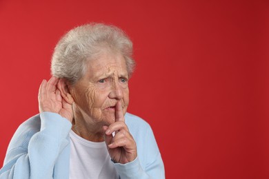 Photo of Senior woman showing hand to ear gesture on red background, space for text