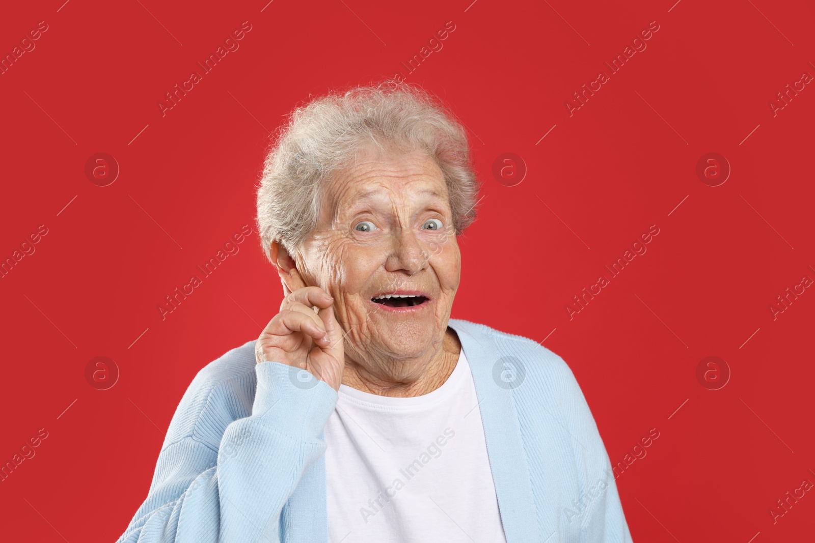 Photo of Senior woman showing hand to ear gesture on red background