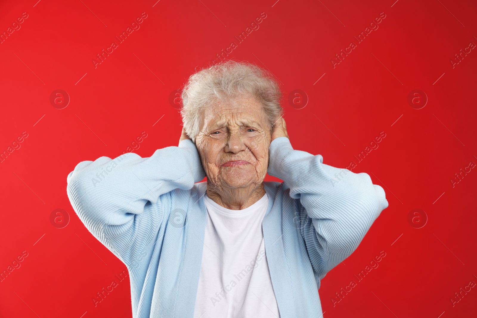 Photo of Senior woman covering her ears on red background