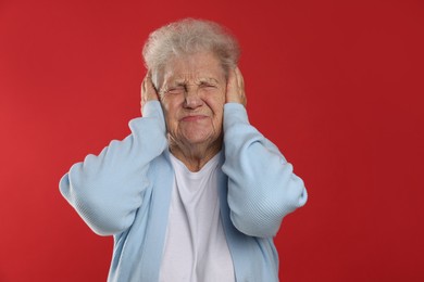 Photo of Senior woman covering her ears on red background