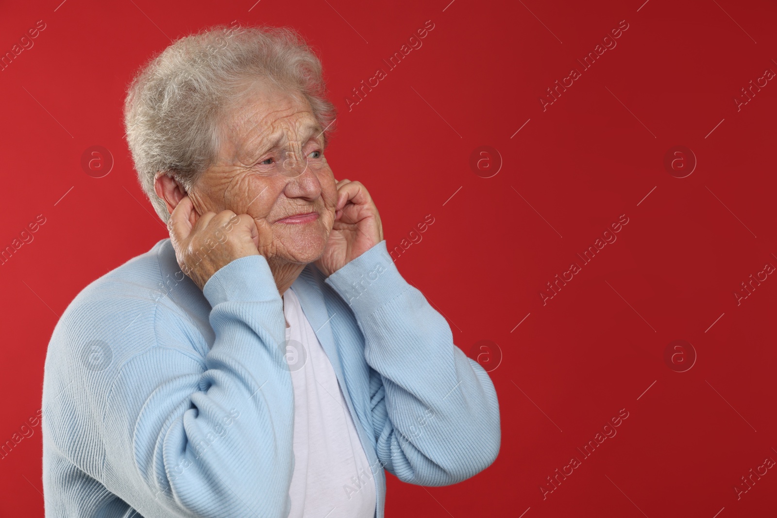 Photo of Senior woman covering her ears with fingers on red background, space for text