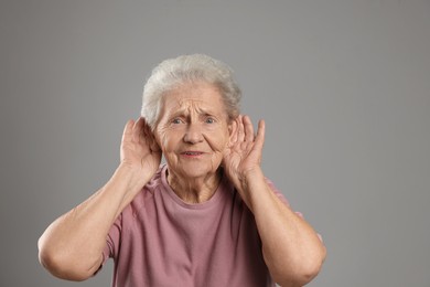 Photo of Senior woman showing hand to ear gesture on grey background