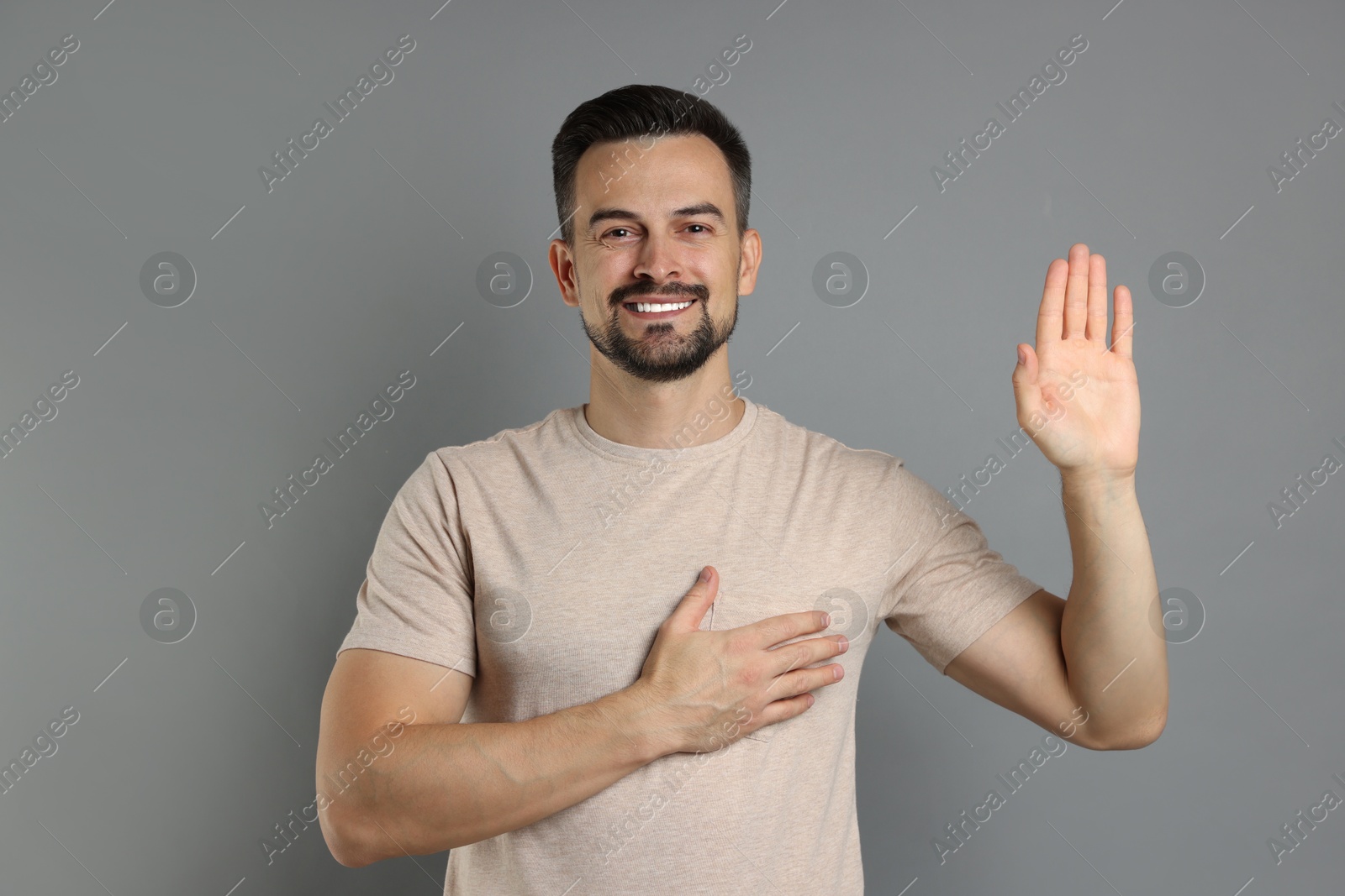 Photo of Man making promise with raised hand on grey background. Oath gesture