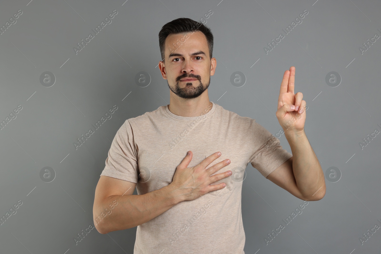 Photo of Man showing oath gesture on grey background. Making promise