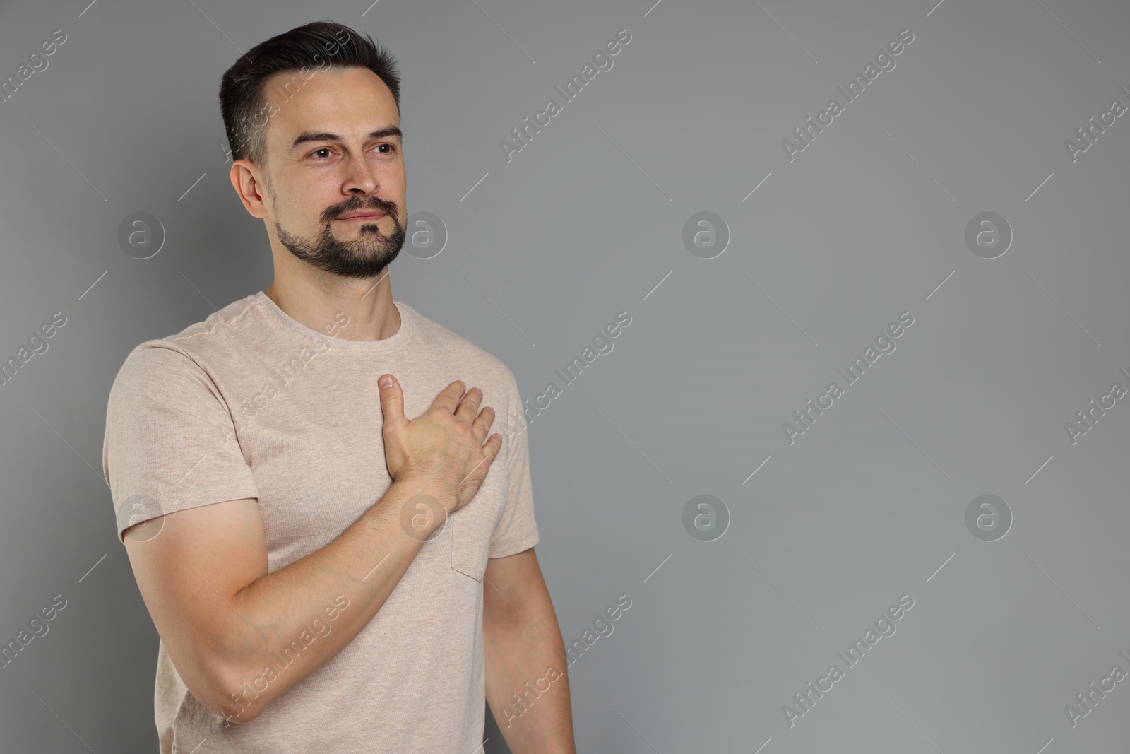 Photo of Man making promise on grey background, space for text. Oath gesture