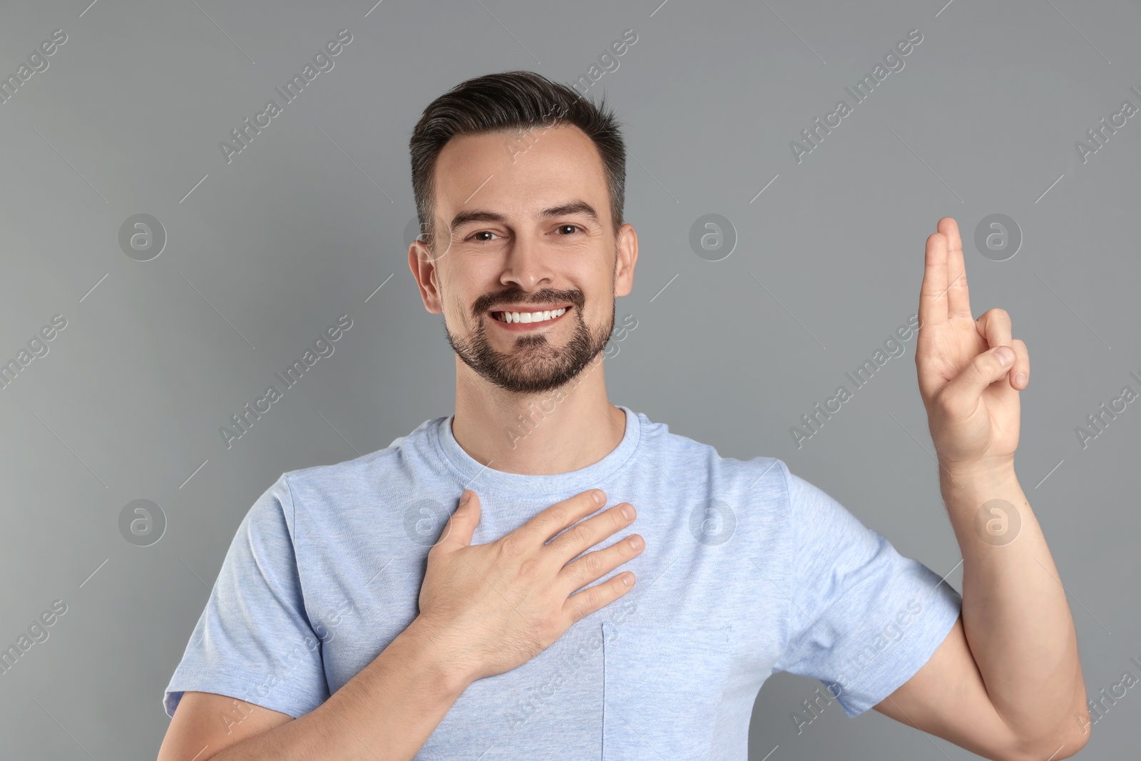 Photo of Man showing oath gesture on grey background. Making promise