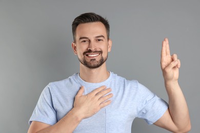 Photo of Man showing oath gesture on grey background. Making promise