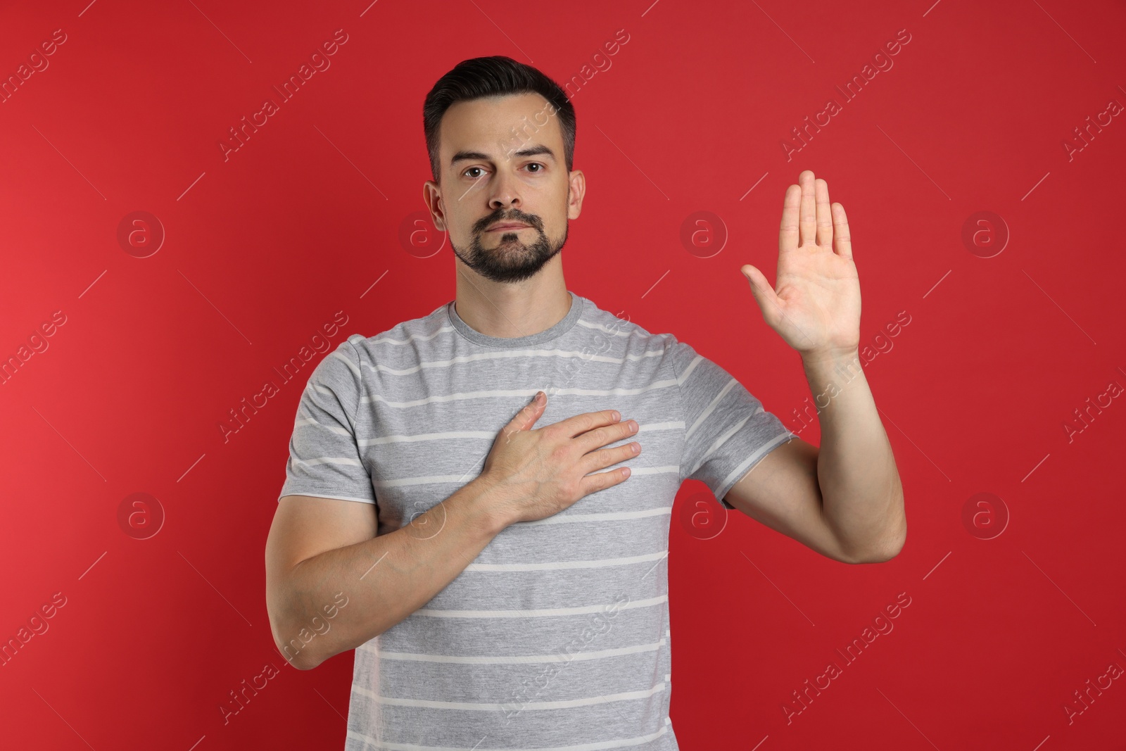 Photo of Man making promise with raised hand on red background. Oath gesture