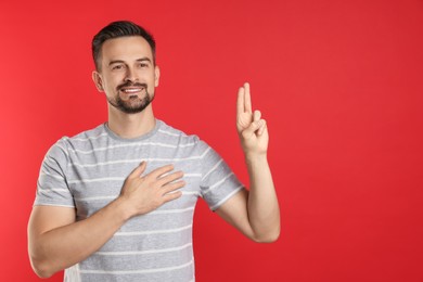 Photo of Man showing oath gesture on red background, space for text. Making promise