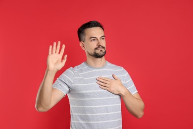 Photo of Man making promise with raised hand on red background. Oath gesture