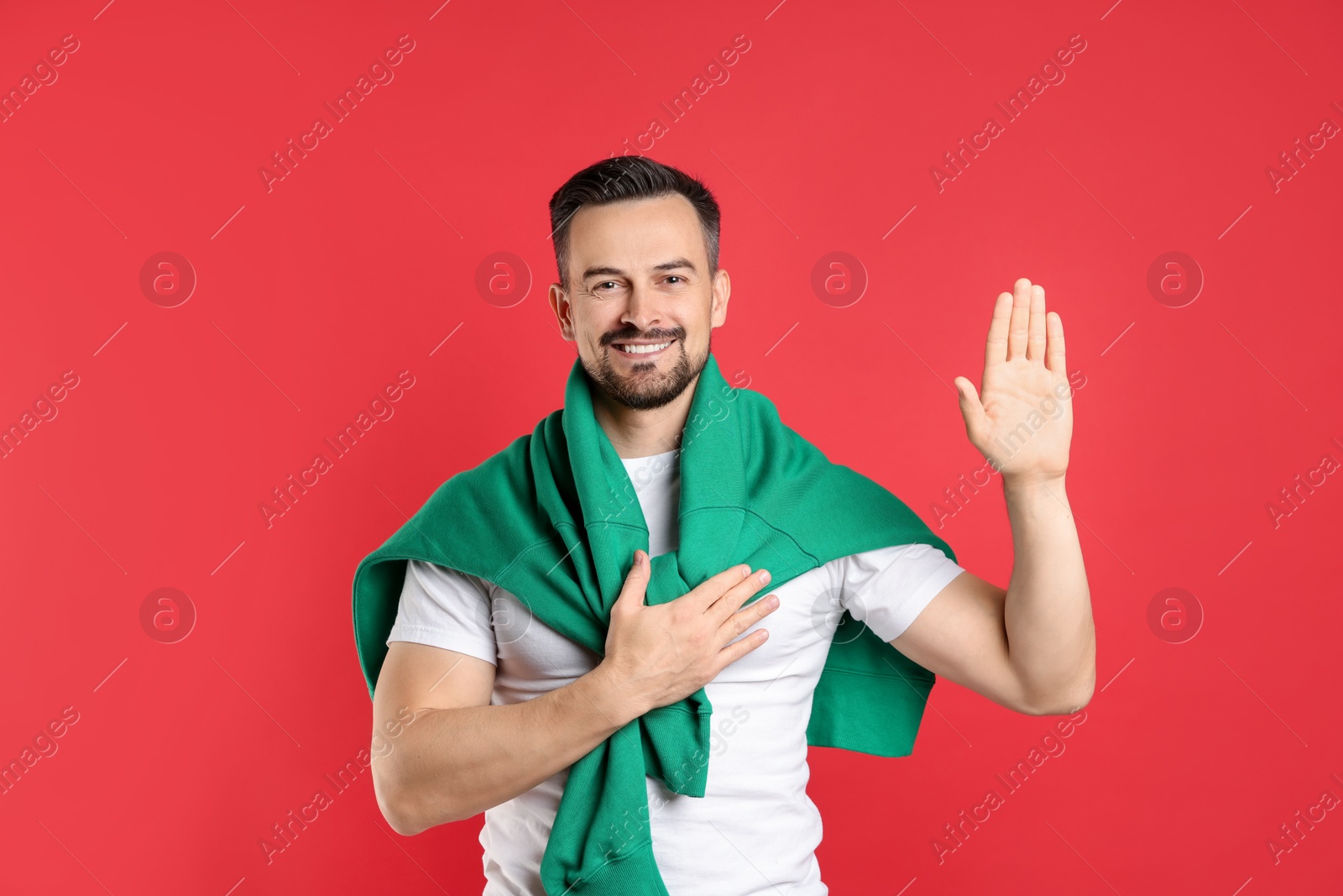 Photo of Man making promise with raised hand on red background. Oath gesture