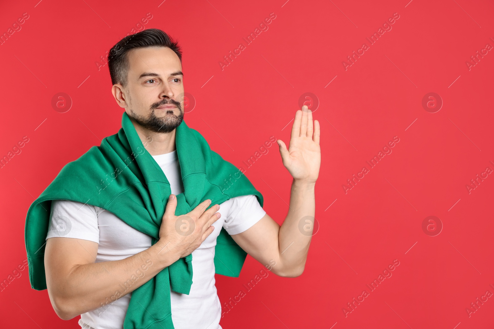 Photo of Man making promise with raised hand on red background, space for text. Oath gesture